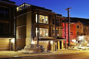 A multi-story building with a garage, a stone foundation, and a well-lit entrance.