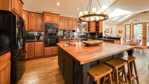 A spacious kitchen with wooden cabinets, a central island with stools, and a large chandelier. - Big Springs by Tahoe Getaways - Luxury Northstar 6 BR - Free Ski Shuttle to Slopes (Truckee)