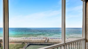 Uitzicht vanaf een balkon op een strand met parasols en een tennisbaan.