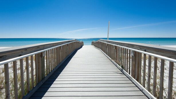 Een houten looppad dat naar een strand leidt, onder heldere luchten.