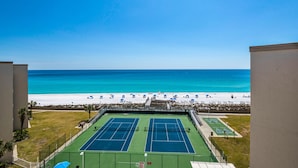 Een tennisbaan met uitzicht op het strand, omgeven door een hek en palmbomen.