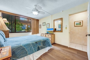 Una camera da letto con un letto, una ventola a soffitto, un comò, un televisore e una finestra vista palme.