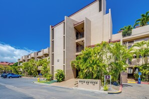 A multi-story hotel with balconies, palm trees, and a clear blue sky.