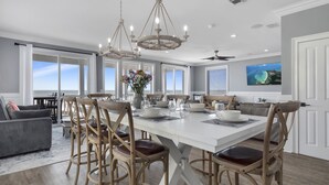 A spacious dining area with a large white table, wooden chairs, and a chandelier.