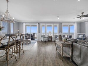 A spacious living room with a large grey sofa, a dining area with wooden chairs, and a view of the ocean through large windows. - San Sou Sea: Amazing 5 BR Beachfront Home- Sleeps 14, Priv. Pool & Hot Tub! (Port St. Joe)