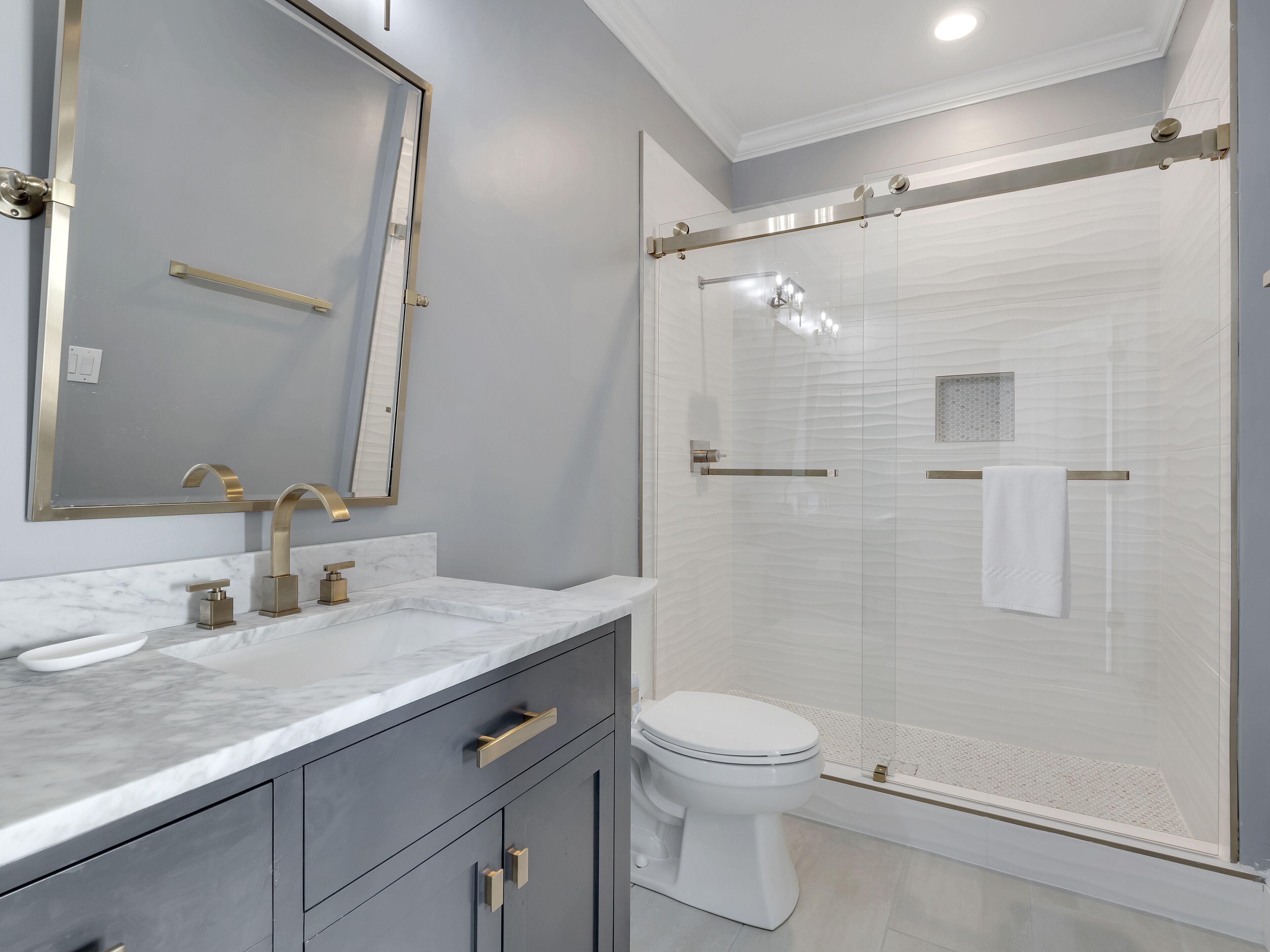 A modern bathroom with a marble vanity, a toilet, and a glass-enclosed shower.