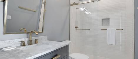 A modern bathroom with a marble vanity, a toilet, and a glass-enclosed shower.