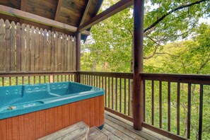 Eine Holzterrasse mit Whirlpool und Blick auf einen Wald.