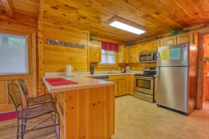 A wooden cabin kitchen with a central island, wooden cabinets, a stainless steel refrigerator, and a microwave. - Pigeon Forge | Pool Table | Hot Tub | WiFi | Resort Pool | Fireplace (PIGEON FORGE)