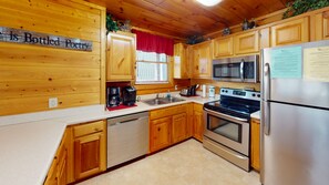 A kitchen with wooden cabinets, a stainless steel refrigerator, a microwave, a stove, and a coffee maker. - Pigeon Forge | Pool Table | Hot Tub | WiFi | Resort Pool | Fireplace (PIGEON FORGE)