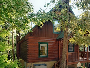 A wooden cabin with a green window, a wooden deck, and a staircase leading to the entrance. - Pigeon Forge | Pool Table | Hot Tub | WiFi | Resort Pool | Fireplace (PIGEON FORGE)