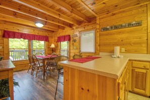 A wooden cabin interior with a dining area, a kitchen with a bar, and a sign reading "Wine is Bottled Poetry". - Pigeon Forge | Pool Table | Hot Tub | WiFi | Resort Pool | Fireplace (PIGEON FORGE)
