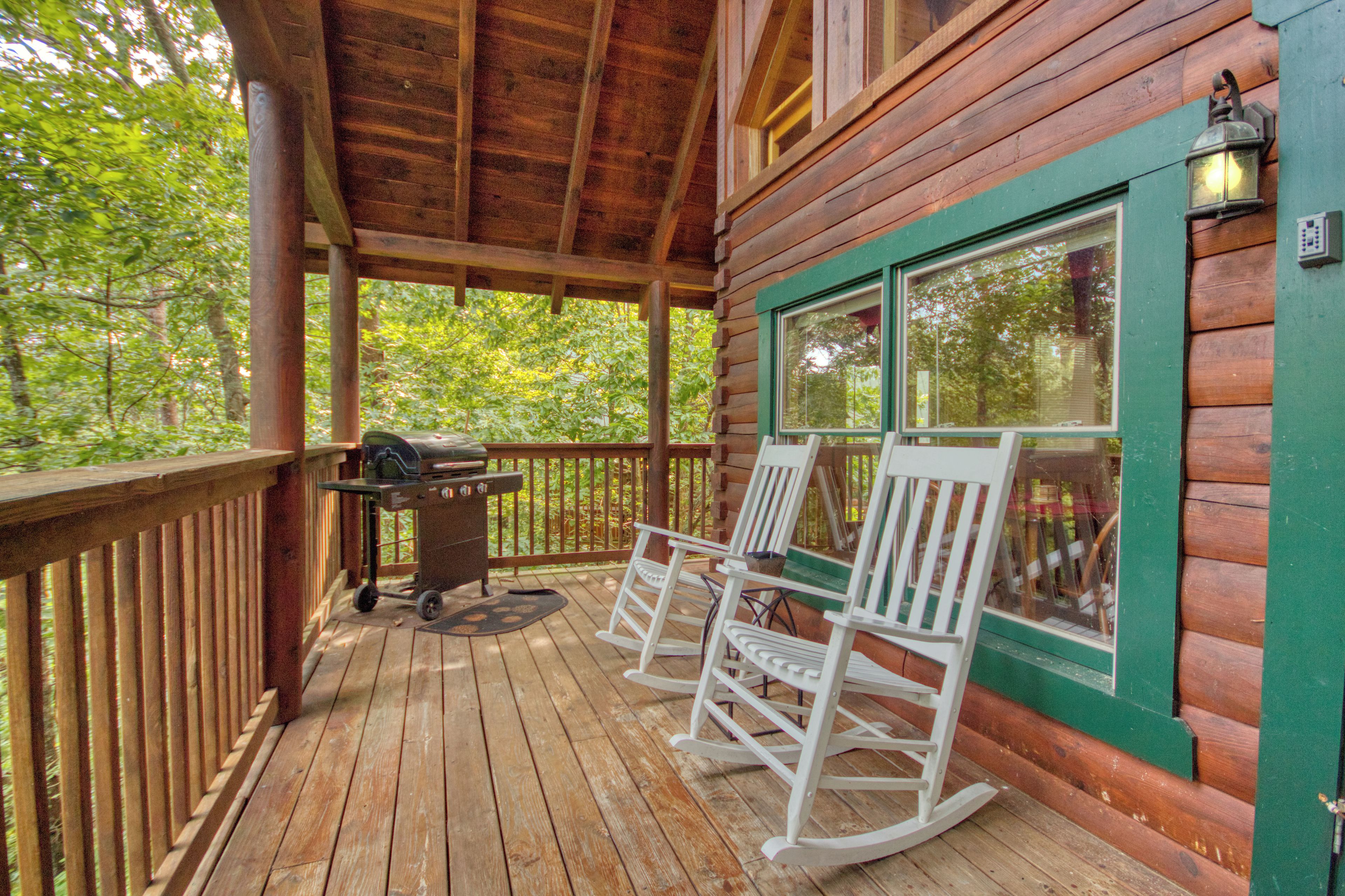 A wooden deck with rocking chairs and a grill, overlooking a forested area.
