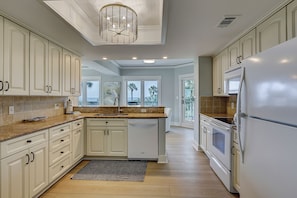 A kitchen with white cabinets, a granite countertop, a built-in dishwasher, and a refrigerator.