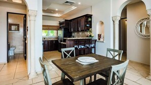 Une cuisine moderne avec des meubles de couleur bois foncé, un îlot central et un coin repas comprenant une table et des chaises en bois.