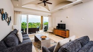 Un salon spacieux comprenant un ensemble de canapés, une table basse, un téléviseur et un balcon avec vue sur la verdure.