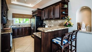 Une cuisine moderne avec des meubles de couleur bois foncé, un plan de travail en granit et un îlot central intégré avec des tabourets de bar.