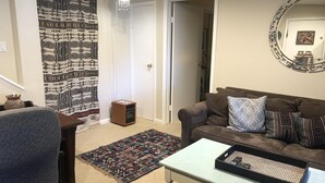 A living room with a brown sofa, a white coffee table, a patterned rug, and a small wooden speaker.