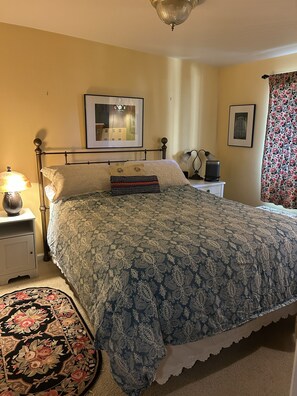 A bedroom with a bed, a nightstand, a lamp, a framed picture on the wall, and a floral curtain.