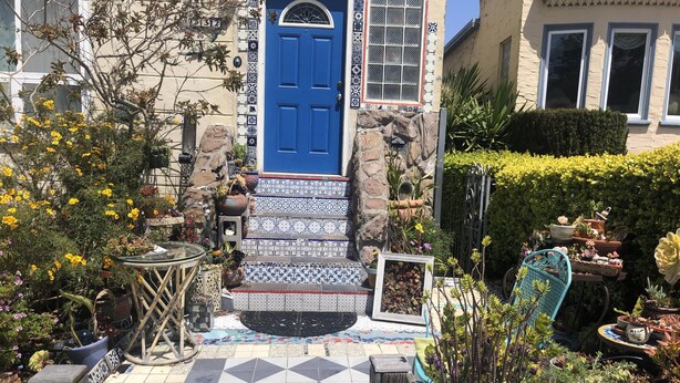 A courtyard with a blue door, patterned tiles, and various potted plants.