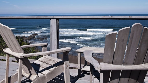 Una terraza de madera con dos sillas Adirondack frente al océano.