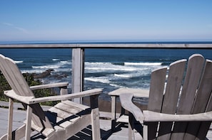 A wooden deck with two Adirondack chairs overlooking the ocean.