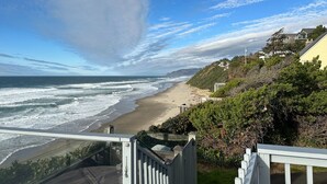 Vista costera desde un balcón con vistas a una playa, olas, cielo despejado y edificios residenciales al fondo.