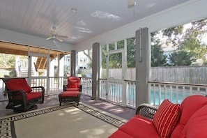 A covered outdoor area with wicker chairs and a red sofa, a ceiling fan, and a view of a swimming pool. - Amazing Island Home, Private Pool, Close to Beach! - 3008 Hartnett (Isle Of Palms)