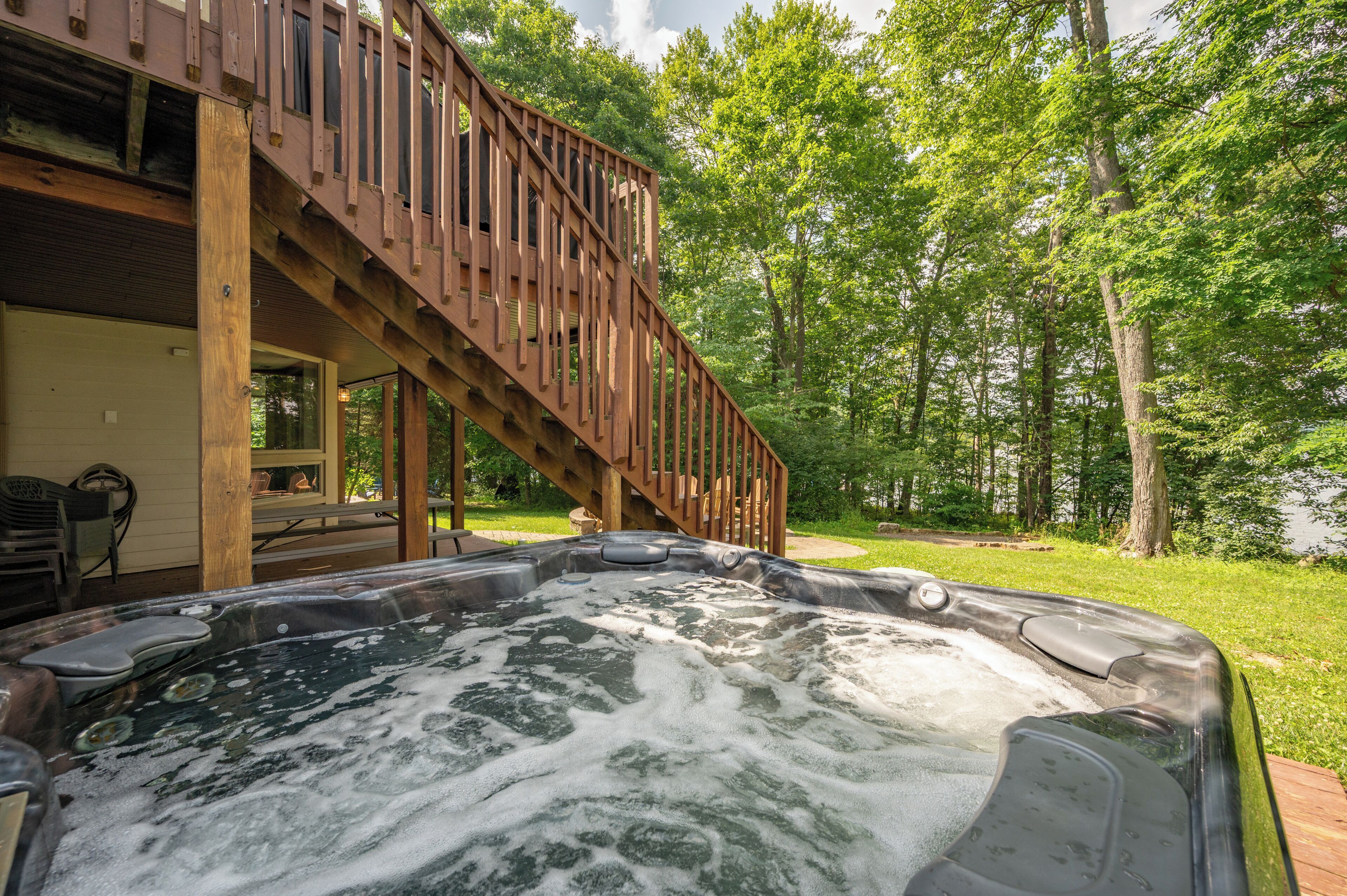 A hot tub with a wooden deck and stairs leading to a covered area.