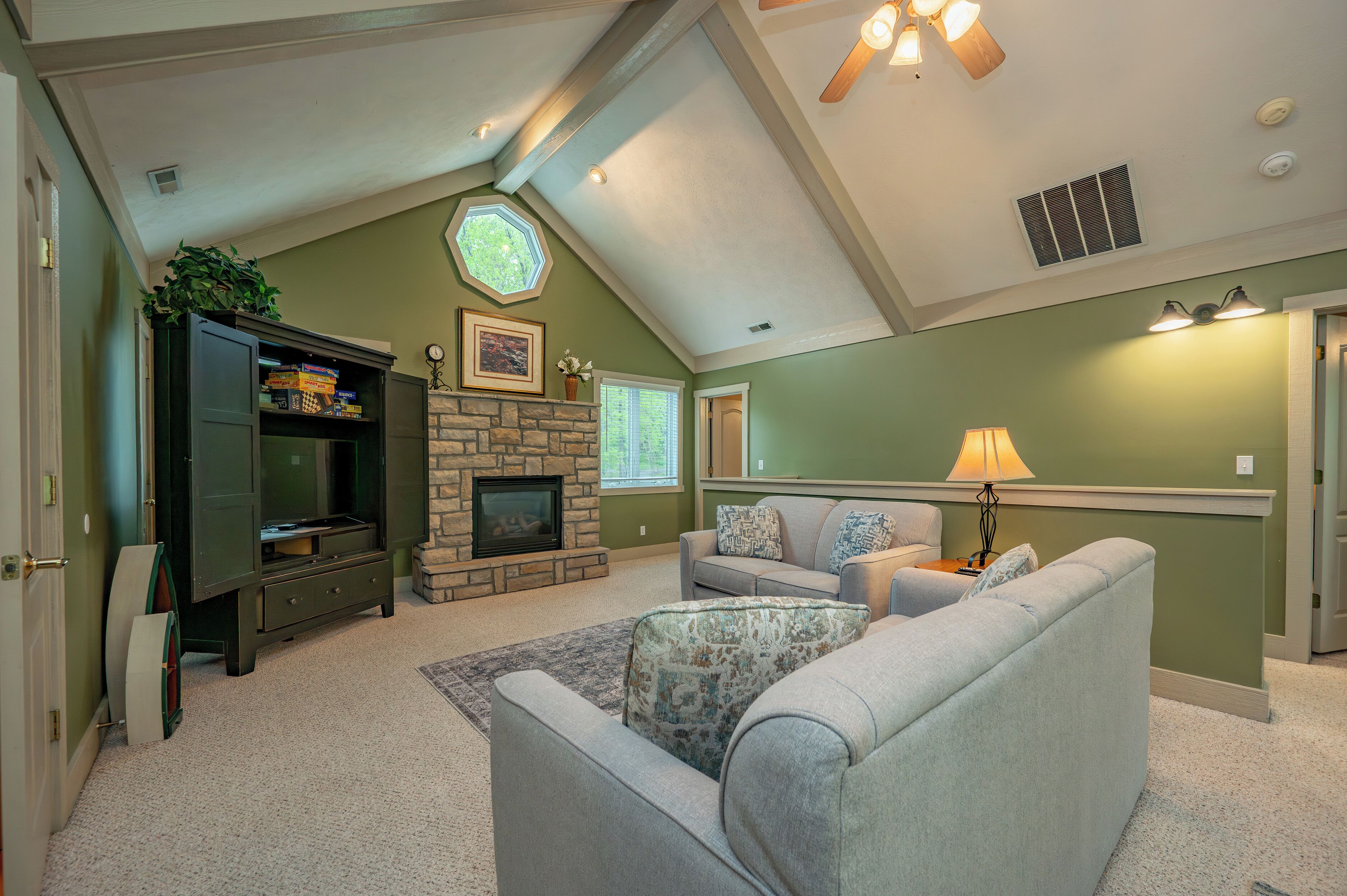 A living room with a stone fireplace, a television, and a ceiling fan.