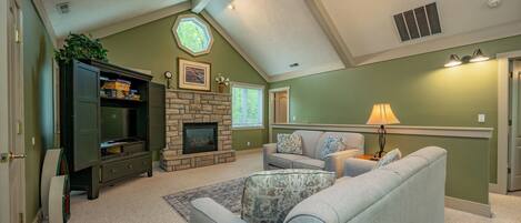 A living room with a stone fireplace, a television, and a ceiling fan.