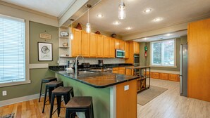 A kitchen with wooden cabinets, a central island with stools, a microwave, and a refrigerator. - Hot Tub, Fire Pit & Stunning Lake Views (Oakland)