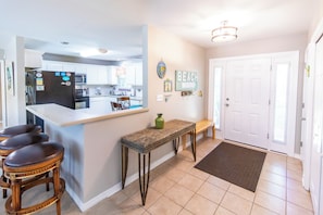 A modern kitchen with a central island, a dining area with a bench, and a door leading to another room.