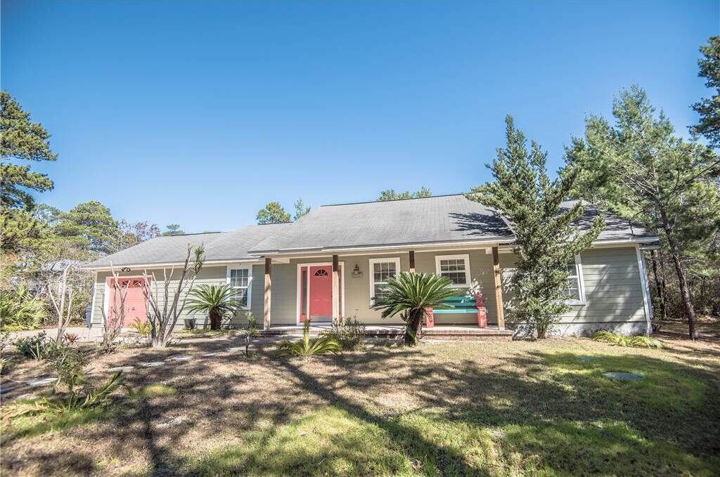 A single-story house with a red door, a covered front porch, and a small front yard with trees and shrubs.