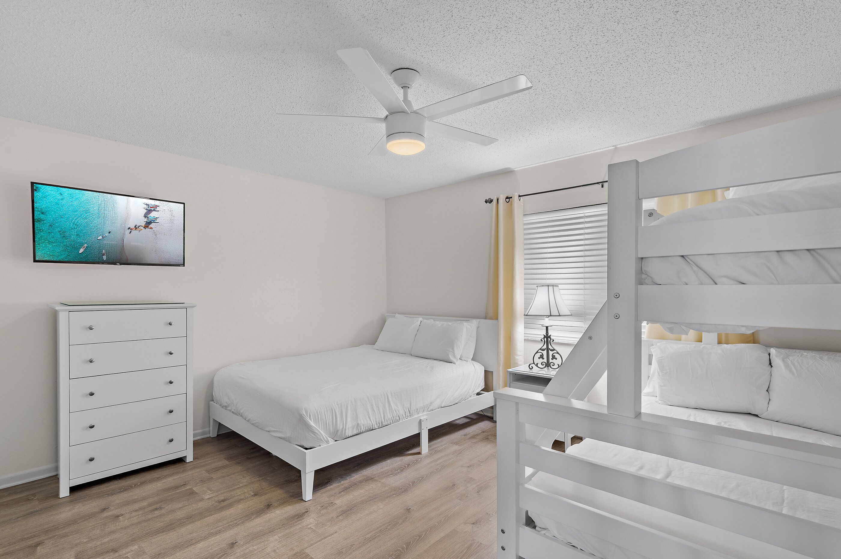 Une chambre à coucher comprenant un lit, une commode, un ventilateur de plafond et un téléviseur fixé au mur.