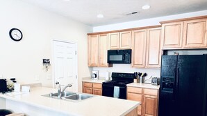 A modern kitchen with wooden cabinets, a black refrigerator, a microwave, and a sink. There are three wooden stools and a clock on the wall. - Fortune's Edge Retreat by Mesquite Vacation Rentals: Ground Level with 2 Car Garage and $510 in free daily activities (Mesquite)