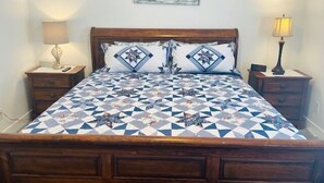 Ein Bett mit geometrisch gemustertem Bettbezug, zwei passende Kissen, einem Holzkopfende und einem an der Wand hängenden abstrakten Gemälde.