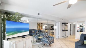 Uma sala de estar ampla, com uma TV de tela plana grande, um sofá confortável e uma mesa de jantar.