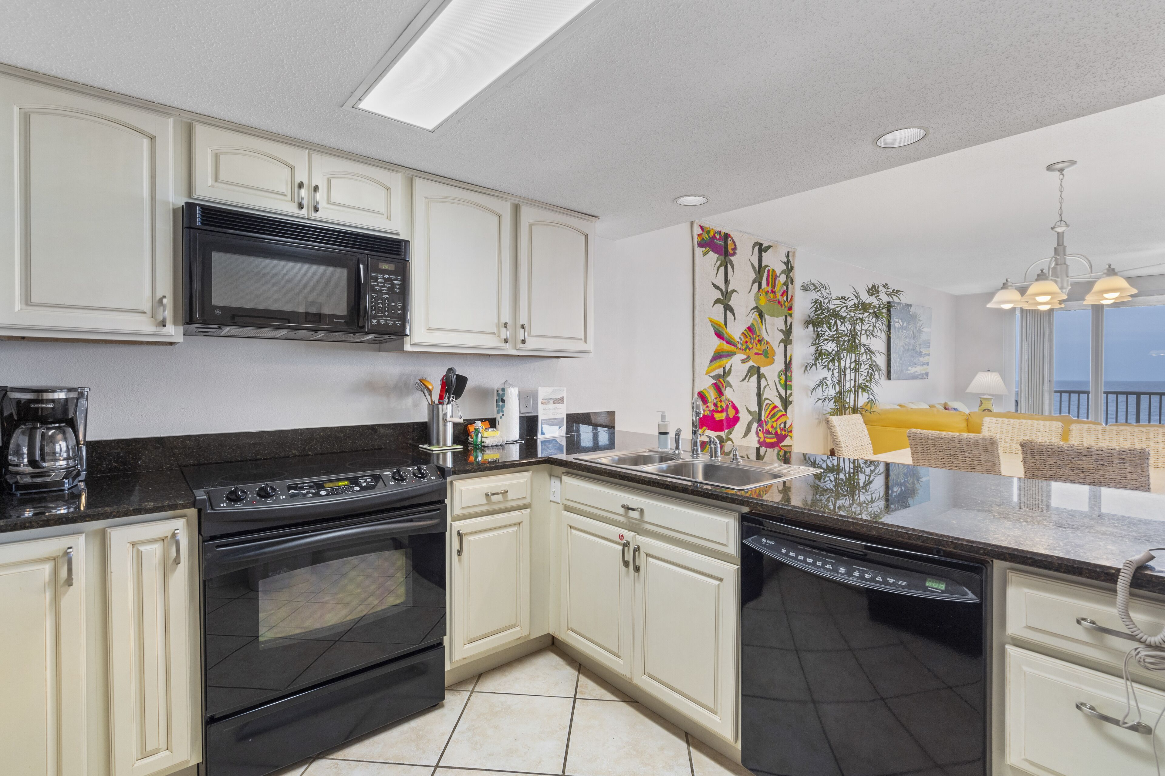 A modern kitchen with white cabinets, a black stove, and a dishwasher. There is a large window providing natural light and a view of the outdoors.
