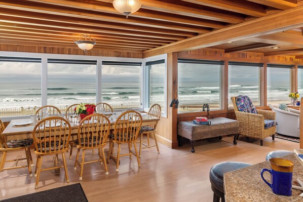 A room with wooden flooring, a dining table with chairs, a bench, and large windows overlooking the ocean. - Stairs to the Sea Sea is on the beach with hot tub. Families love this house. (Lincoln City)