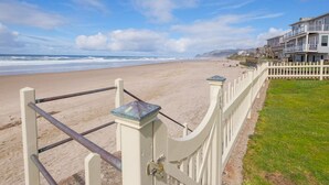 A beach view with a white fence and houses in the background. - Steps to the beach, hot tub, sand toys, families love this house. (Lincoln City)