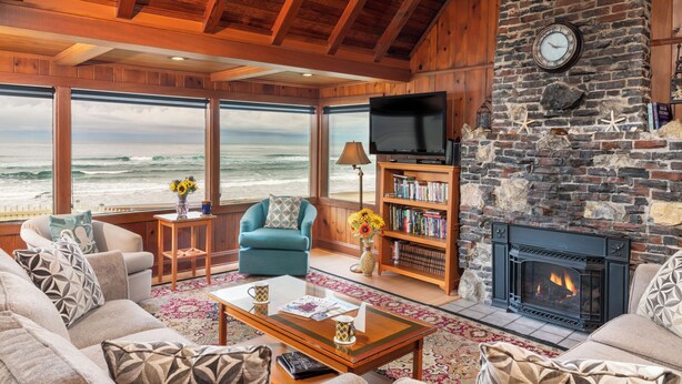 A cozy living room with a fireplace, large windows overlooking the ocean, comfortable seating, and a bookshelf. - Steps to the beach, hot tub, sand toys, families love this house. (Lincoln City)