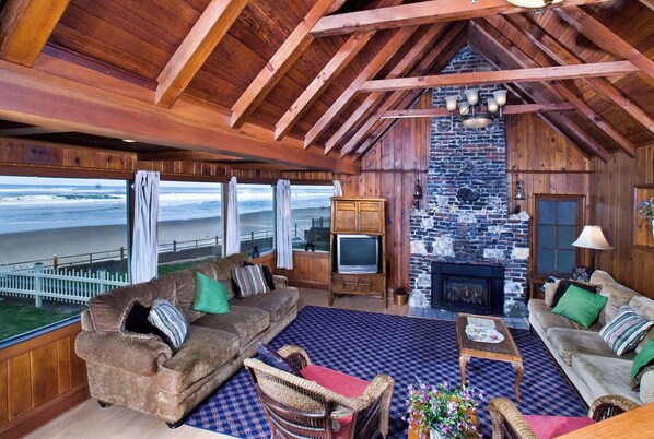 Relax in this cabin's cozy seating area, featuring a leather sofa and armchair, stone fireplace, and ocean views.
