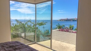 Ein Schlafzimmer mit einer großen Schiebeglastür, die auf einen Balkon mit Blick auf das Meer und eine entfernte Insel führt.