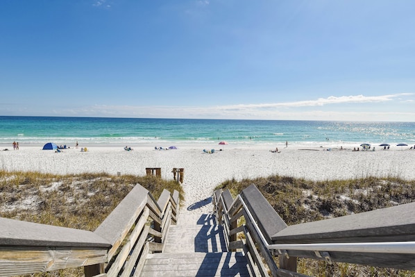 A beach with a wooden boardwalk leading to the water, sandy beach, and tents.