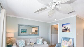 A living room with a ceiling fan, a sofa, a coffee table, a chair, a lamp, and artwork on the walls. - Serene Condo w/ Stunning Gulf Views on Scenic 98 in Miramar Beach! 🌊☀🏖 (Miramar Beach)