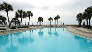A swimming pool with lounge chairs and palm trees, surrounded by a fence. - Master Gulf View Upgraded in 2023 Free round of Golf & Activities Every Day! (Panama City Beach)