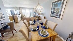 A dining area with a wooden table set for six, featuring blue glassware and decorative plates. - Master Gulf View Upgraded in 2023 Free round of Golf & Activities Every Day! (Panama City Beach)