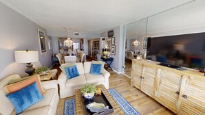 A modern living room with a sofa set, a coffee table with decorative items, a television, and a mirrored wall. - Master Gulf View Upgraded in 2023 Free round of Golf & Activities Every Day! (Panama City Beach)