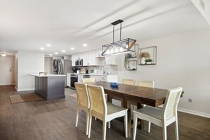 A modern kitchen with white cabinets, stainless steel appliances, and a wooden dining table with four chairs.